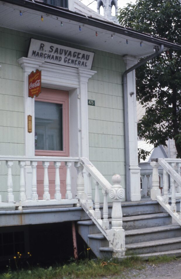 Photo de la porte rose d'un magasin général. Au-dessus de la porte il est inscrit « R. Sauvageau - marchand général ».