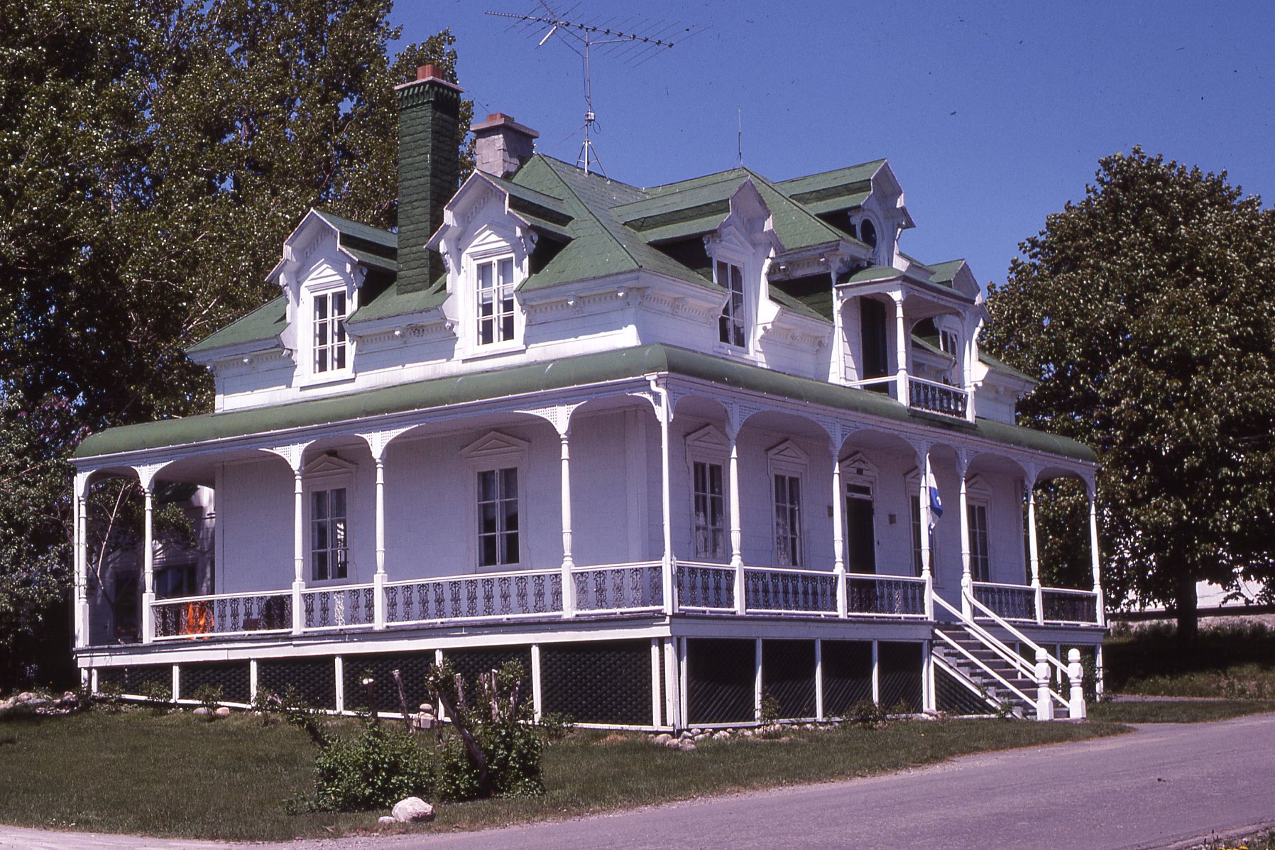 Maison blanche au toit vert à quatre versants.