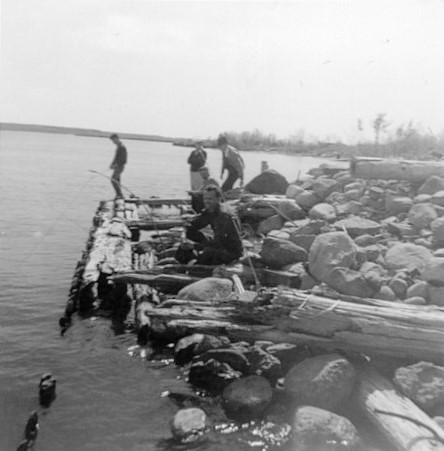 Photo en noir et blanc de cinq hommes pêchant au bout du quai. 