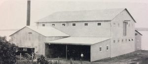 Black and white photo of a factory on the water's edge.