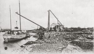 Black and white photo of a quarry on the water's edge and a boat being loaded.