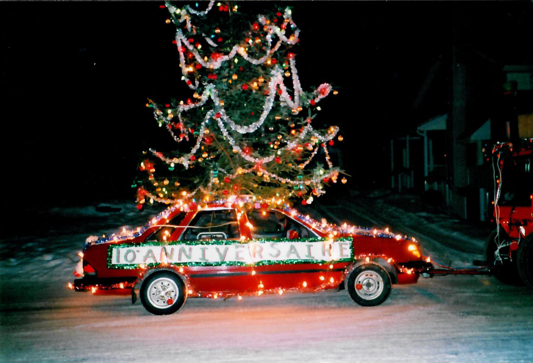 Voiture rouge décorée de lumières et d'un de Noël sur son toit. Il est inscrit « 10e anniversaire ».