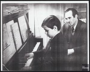 Photo en noir et blanc de André Mathieu assis au piano avec son père Rodolphe. 