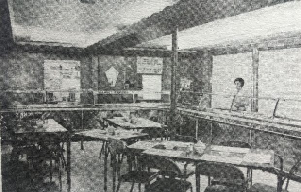 Photo en noir et blanc de l'intérieur de la cafétéria du restaurant la Petite vache. Deux dames sont derrière le comptoir. 