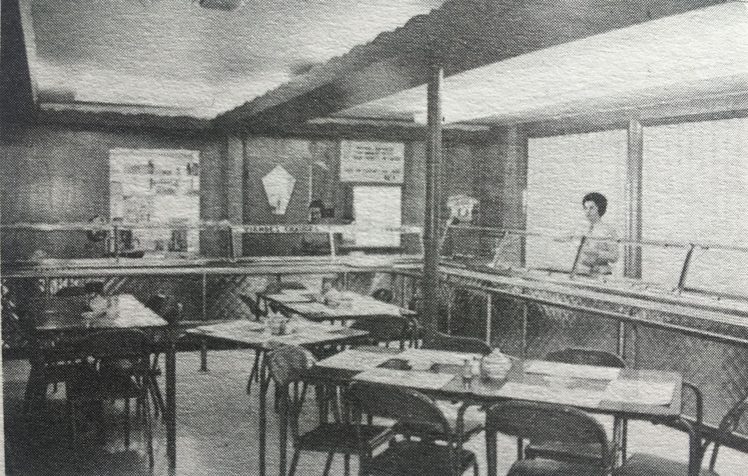 Photo en noir et blanc de l'intérieur de la cafétéria du restaurant la Petite vache. Deux dames sont derrière le comptoir. 