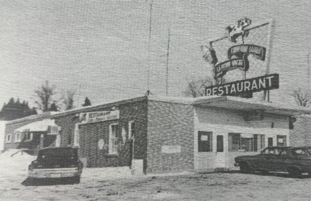 Photo en noir et blanc d'un bâtiment avec une insigne mentionnant  Restaurant et deux voitures stationnées devant. 