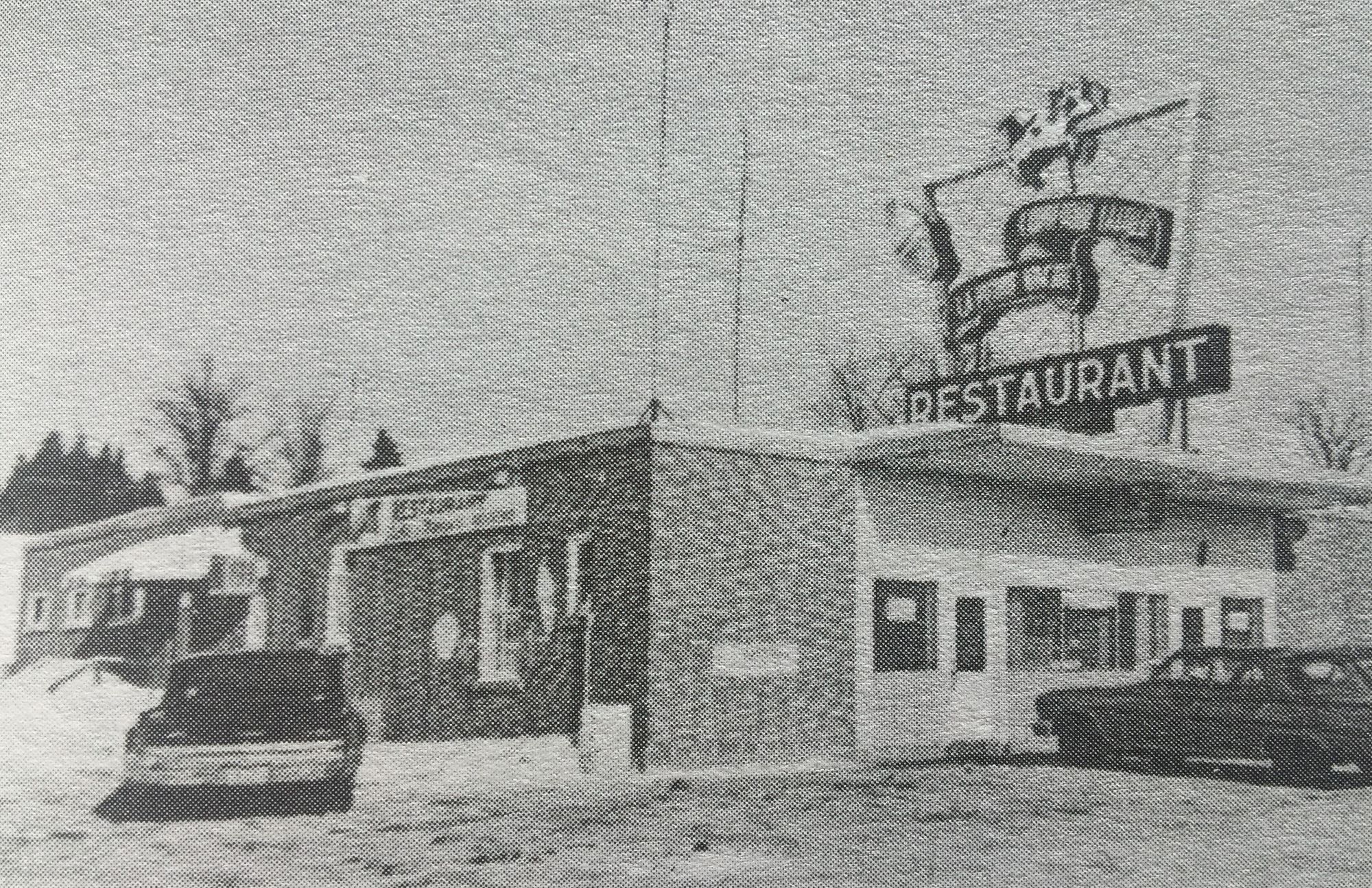 Photo en noir et blanc d'un bâtiment avec une insigne mentionnant " Restaurant" et deux voitures stationnées devant. 