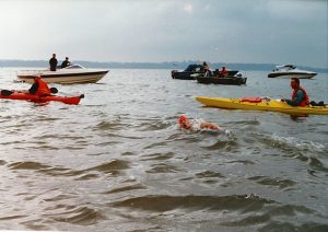 A swimmer, surrounded by two kayaks and four motorboats, swims across the river.