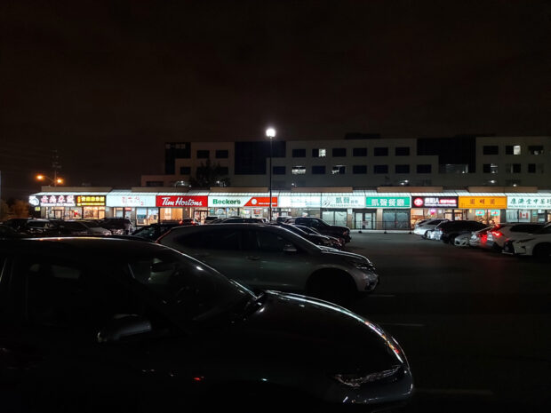 Une vue nocturne d'un centre commercial d'un étage bien éclairé, avec diverses devantures de magasins, dont Tim Hortons et Beckers, parmi d'autres, avec des caractères asiatiques sur leurs enseignes.