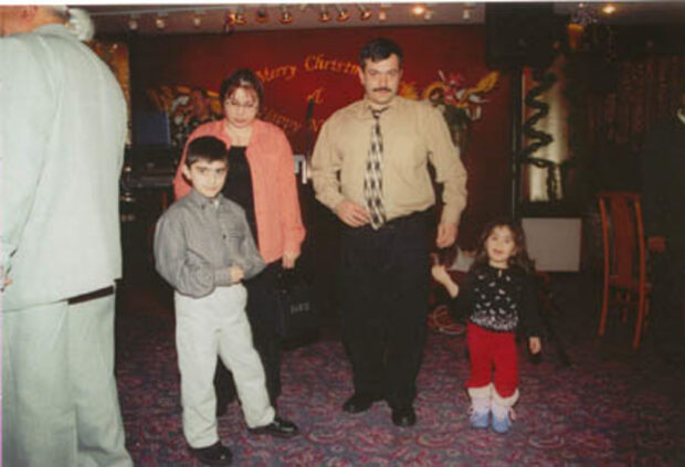 Une photographie analogique représentant deux adultes et deux jeunes enfants dans un restaurant avec derrière eux une banderole indiquant Joyeux Noël