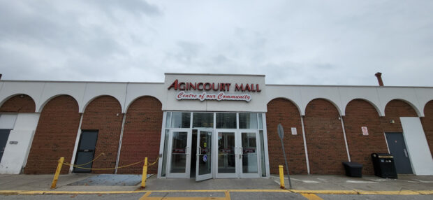 L'entrée principale du Agincourt Mall, écrite en grandes lettres rouges avec le sous-titre centre de notre communauté sur une étiquette blanche, entourée d'arches blanches sur un bâtiment d'un étage en briques rouges.