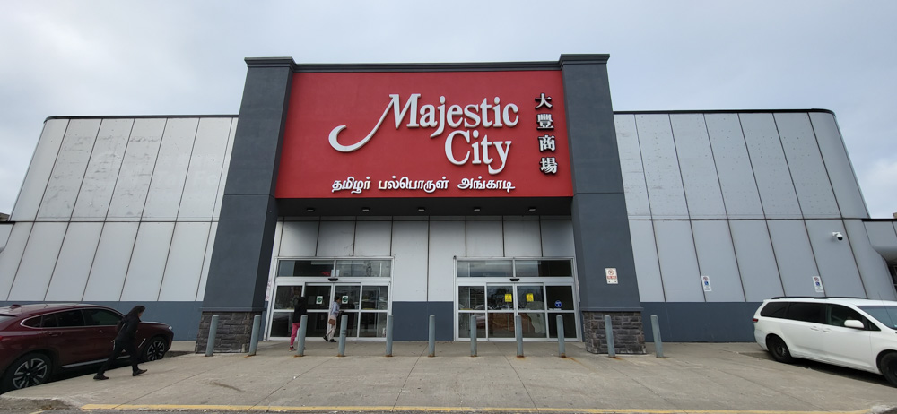 Entrée principale du Majestic City Mall avec un grand panneau rouge affichant le nom du centre en anglais et en caractères asiatiques, sous un ciel nuageux.