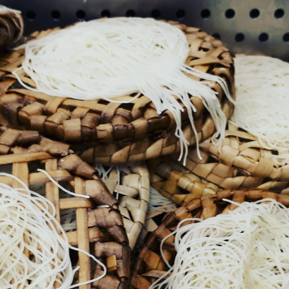 Un gros plan d'un panier d'osier en bambou tressé contenant des nids de nouilles de riz blanches et fines.