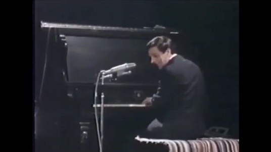 Photo couleur de Claude Léveillée assis au piano de dos.