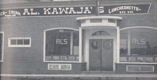 Photo d’extérieur en noir et blanc. Le bâtiment en briques indique Ice-cream Parlor; Al. Kawaja’s; Luncheonette Etc. Etc. Les deux fenêtres principales de chaque côté de la porte d’entrée indiquent également Al’s. Il y a un petit toit au-dessus des portes d’entrée.