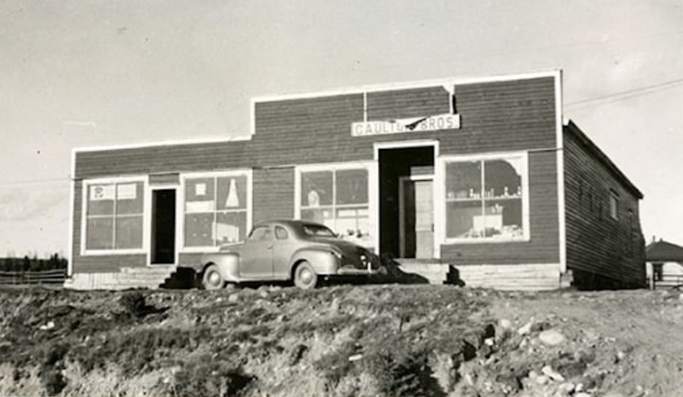 Photo d’extérieur en noir et blanc. Bâtiment de couleur foncée avec quatre grandes fenêtres, deux portes avec escaliers et une fausse façade. L’enseigne au-dessus de la porte principale indique Gaultois Bros. Une voiture est stationnée devant le bâtiment. Un autre bâtiment est visible à droite derrière celui-ci.