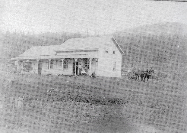 Maison en bois et charettes devant coline boisée