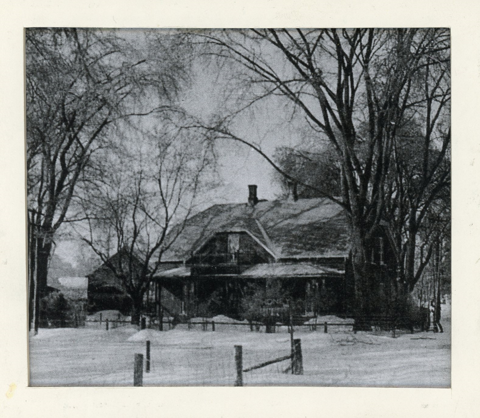 Photographie d’Elmbank, la résidence de Maude Abbott, en hiver, noir et blanc. Il s’agit d’une maison en briques de deux étages avec un toit à deux versants, deux cheminées et une galerie aux deux étages. On aperçoit une clôture en bois à l’avant de la maison, une affiche avec l’inscription « HONEY » devant celle-ci et beaucoup d’arbres sur le terrain. 