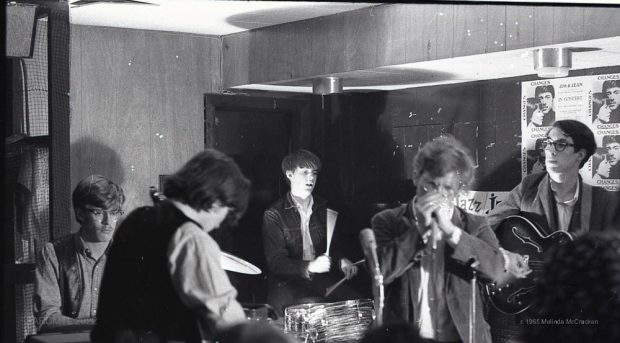 Photographie en noir et blanc de cinq musiciens jouant dans un coin d'une pièce lambrissée.