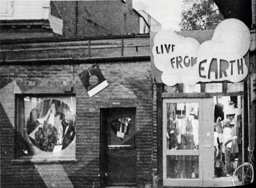 Photographie en noir et blanc d'une devanture de magasin avec une enseigne faite à la main avec le nom du magasin en lettres arrondies épelant Live from Earth.