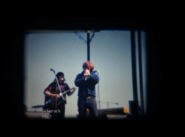 Deux membres du groupe musical Sidetrack apparaissent au centre d'une capture d'écran d'une vidéo de leur performance en plein air dans un parc de Montréal.