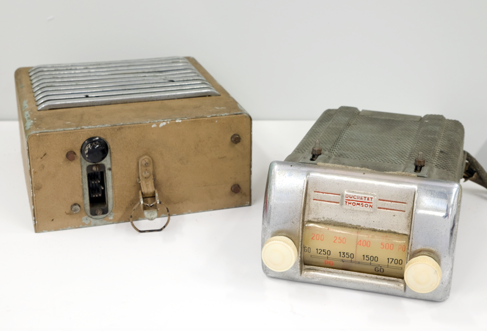La radio en métal argenté possède deux boutons de couleur ivoire et affiche les numéros de fréquence sur le cadran. À gauche de la radio, vous voyez le boîtier de haut-parleur détaché de couleur beige et métal avec une sortie de câble et un mécanisme de fixation sur sa partie inférieure.