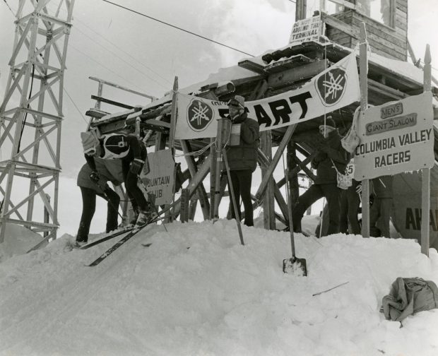 Photographie en noir et blanc d’un skieur prenant son élan d’un portillon de départ.