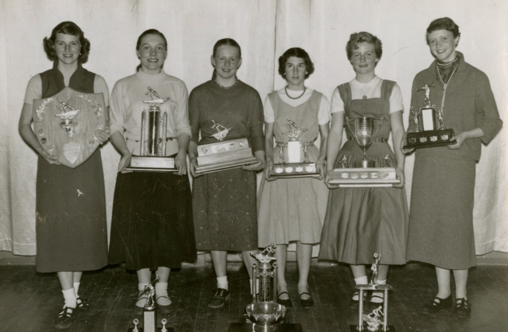 Six jeunes filles tenant des trophées. Trois trophées supplémentaires sont posés par terre devant le groupe.