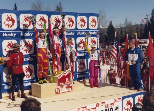 Quatre skieuses sur un podium brandissant leurs fleurs devant une bannière Husky.