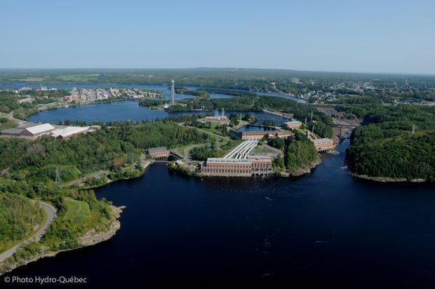 Vue aérienne de Shawinigan qui couvre la baie, les chutes et trois centrales hydroélectriques. Au loin, on retrouve le centre-ville et la tour de La Cité de l’énergie qui se dresse sur une île au milieu de la rivière.