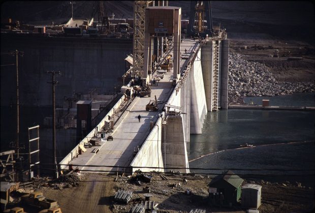 Photographie en gros plan d’un barrage en construction, presque achevé. Des personnes et des véhicules de construction se trouvent sur le barrage.