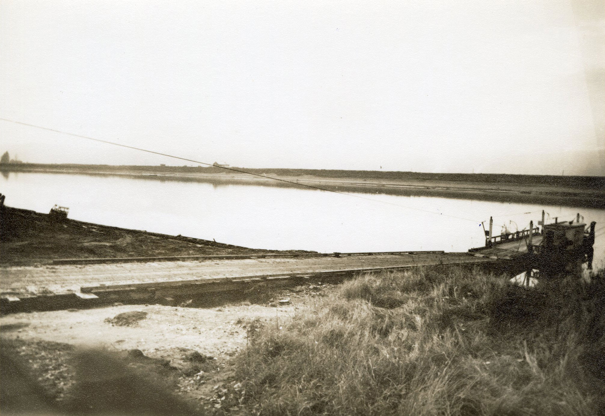 Photographie aux tons sépia d'un traversier amarré au bord de l'eau, avec une rampe d'embarquement menant au traversier.