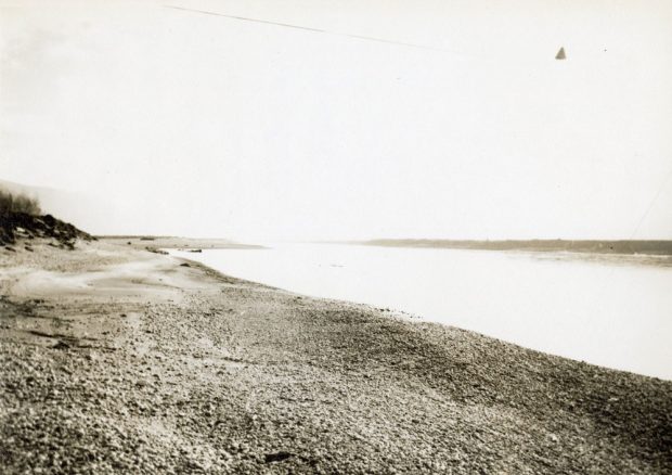 Photographie de paysage aux tons sépia d'un plan d'eau bordé de parcelles de terre.