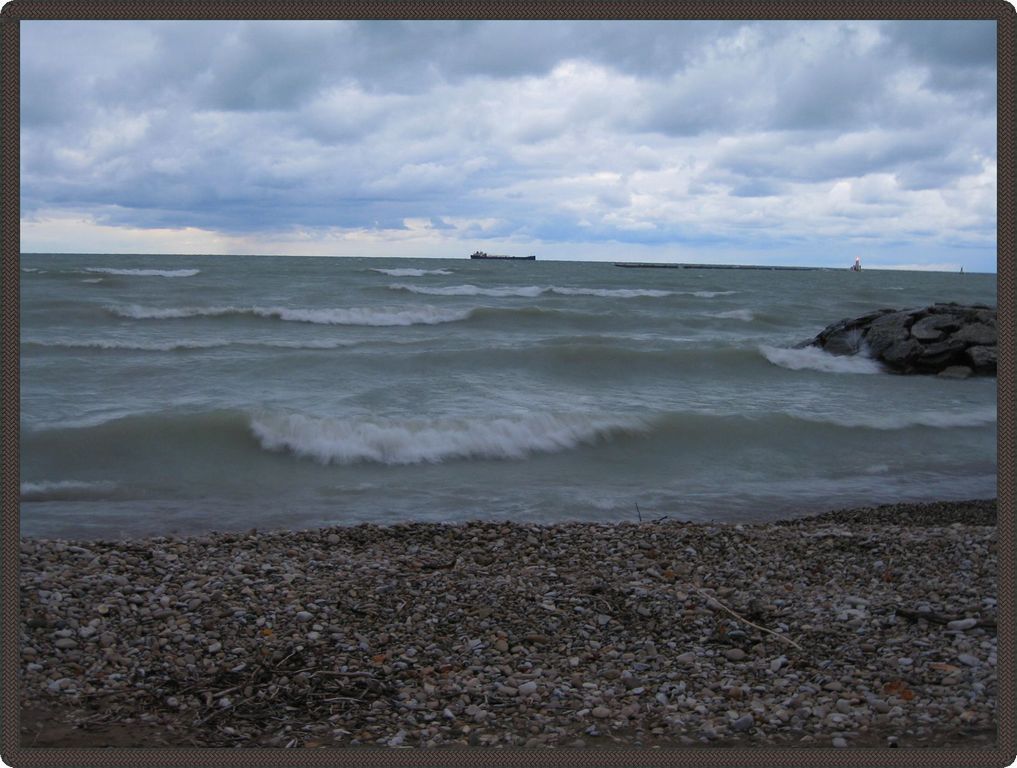 Photo prise à quelques mètres de l’eau, montrant les vagues du lac. Au loin, on aperçoit un grand bateau.