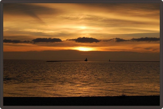 Photo prise au niveau de la plage montrant le ciel orangé partiellement obscurci par les nuages au-dessus du lac.