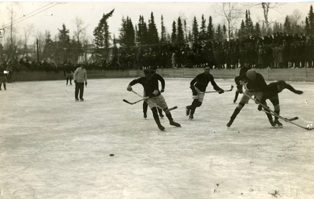 Photographie noir et blanc d'une partie de hockey extérieure.