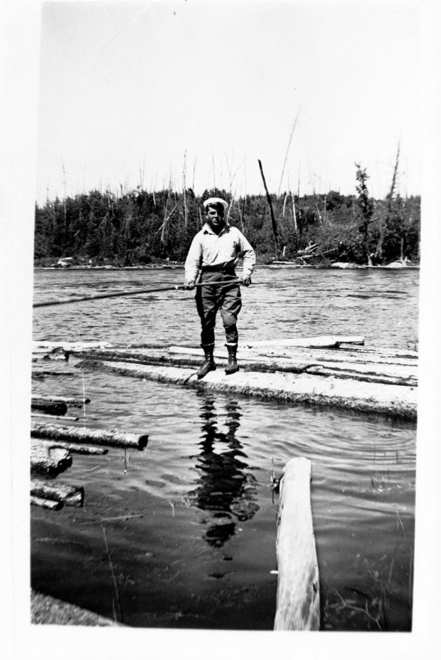 Photographie noir et blanc d'un draveur en équilibre sur un billot en flottaison.