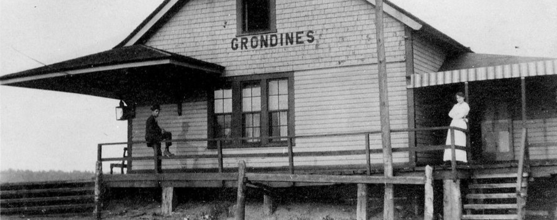 Photo en noir et blanc d'une femme debout et d'un homme assis sur la galerie de la gare de Grondines.